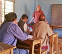 Teacher at chalkboard in class with students sitting at desks.